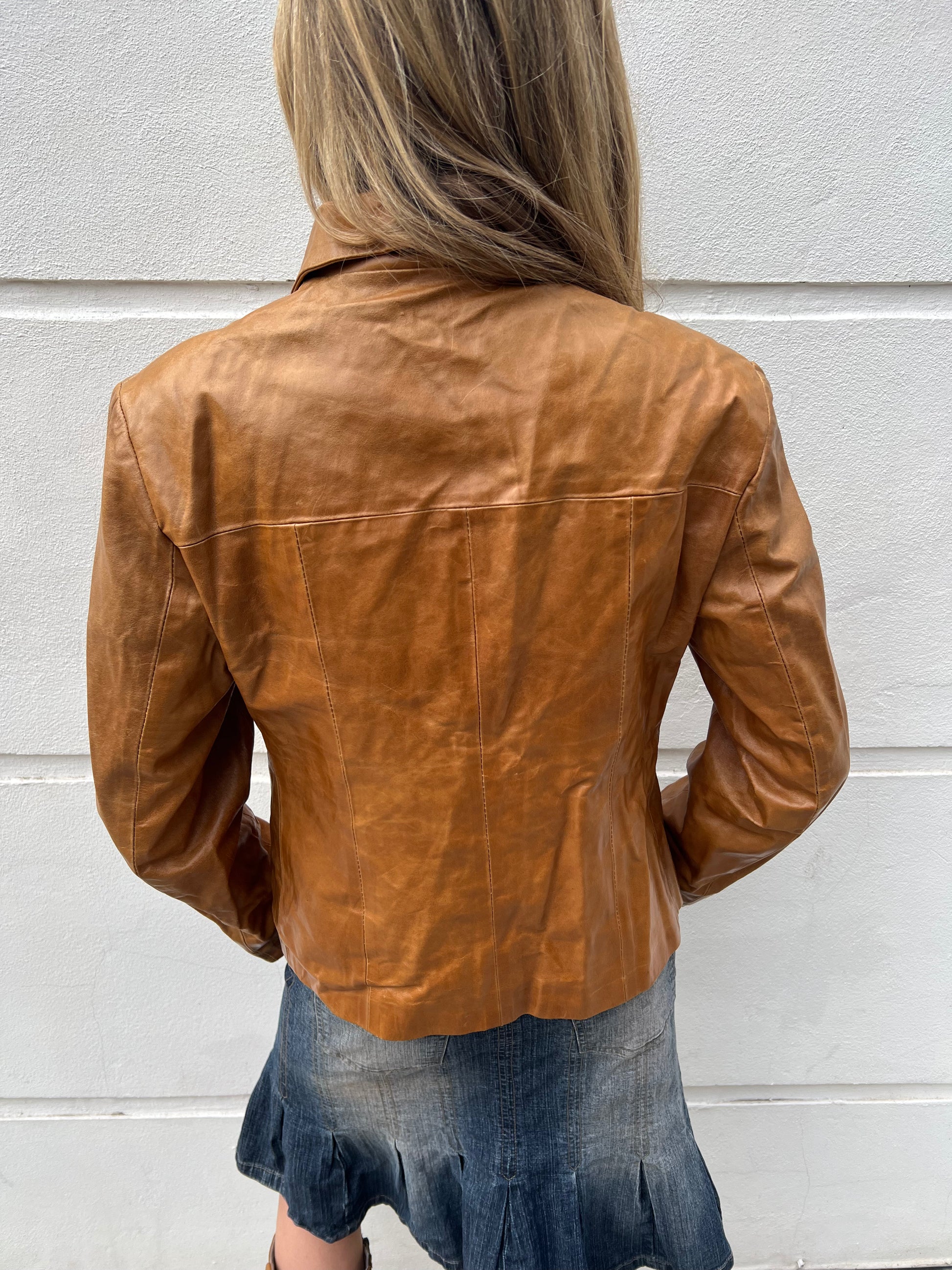 Person wearing a brown leather jacket against a light gray wall