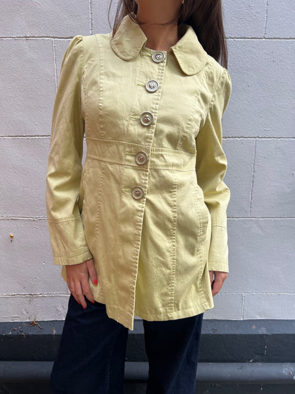 Person wearing a light yellow peacoat against a gray wall.