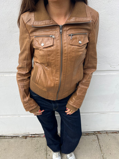 Person wearing a brown leather jacket against a white wall.