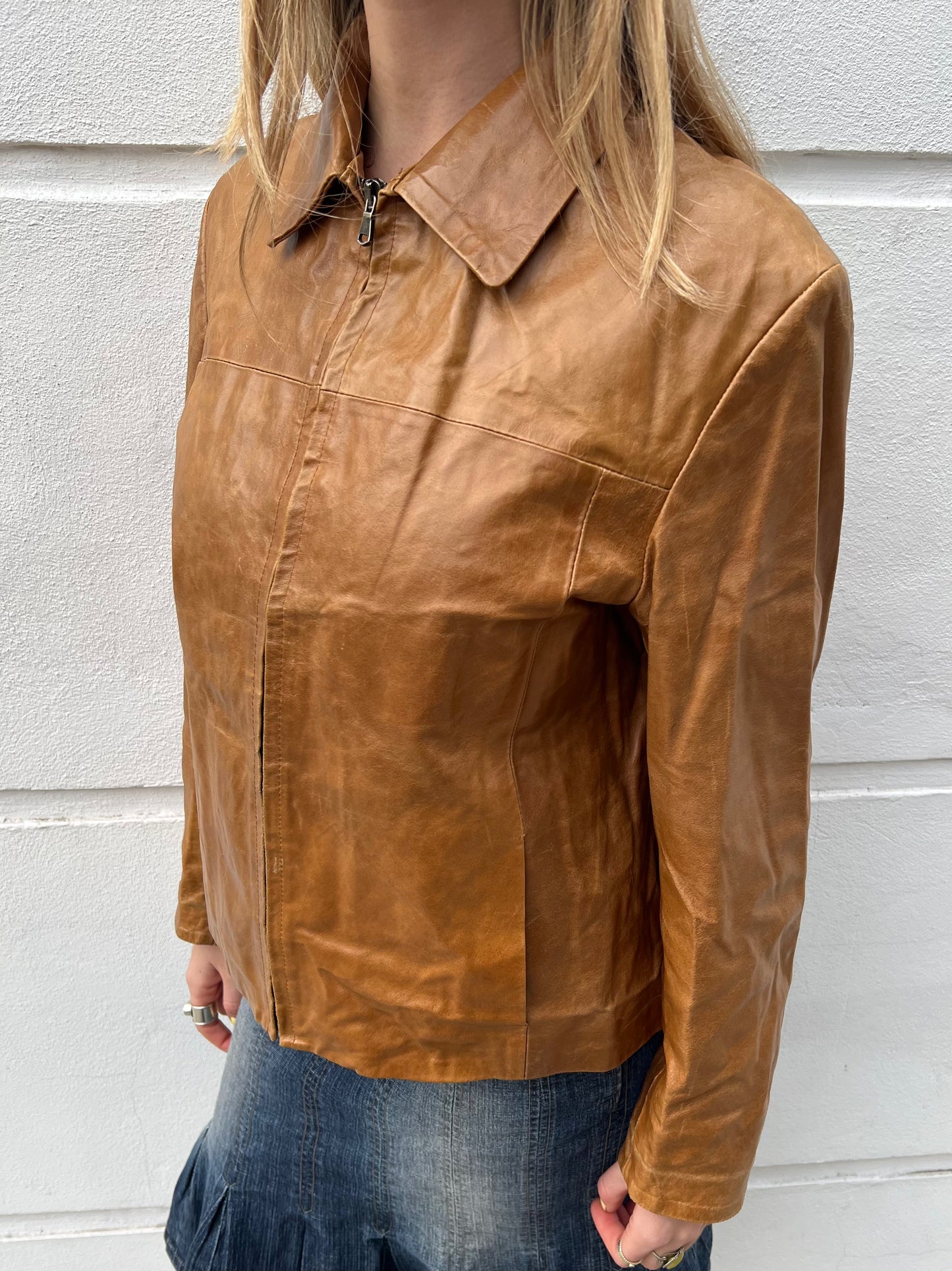 Brown leather jacket worn by a person against a light gray wall.